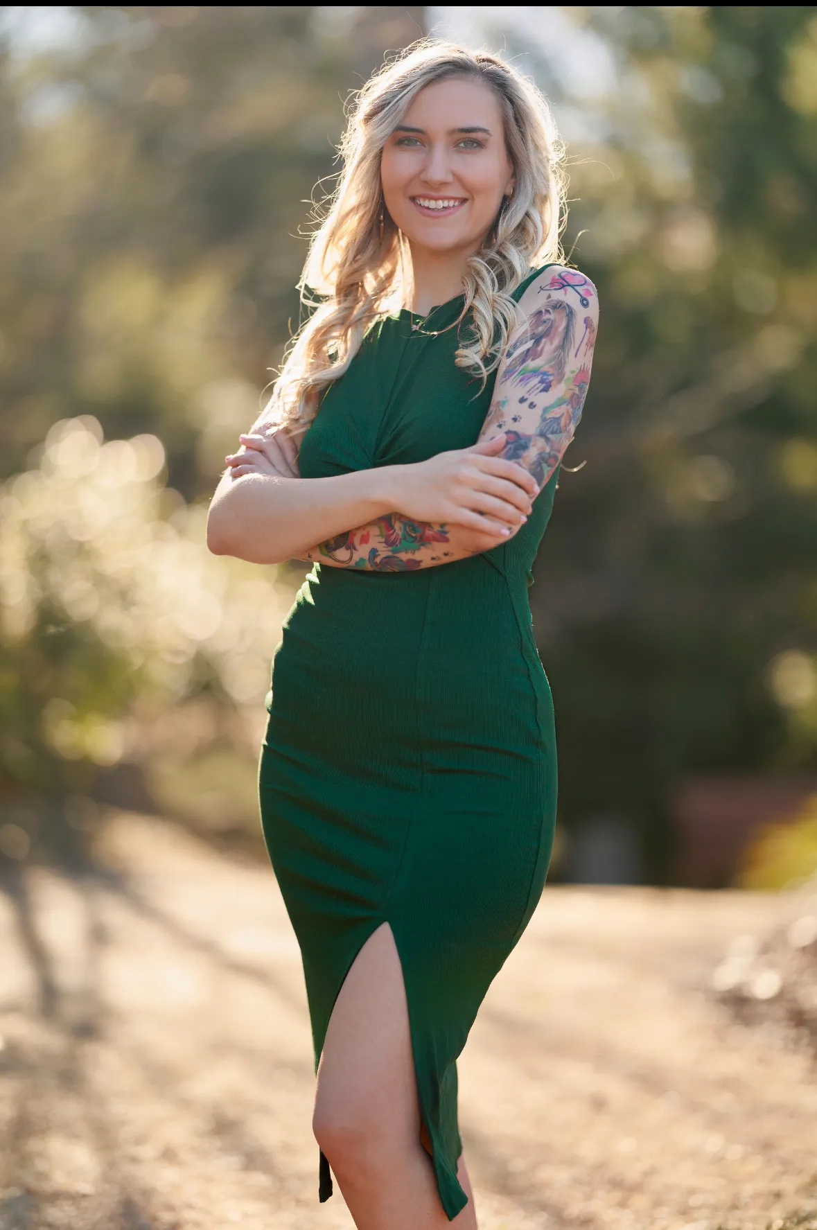 Kière Joi, founder of Rhinestone Dance Co., standing with arms crossed, tattoo sleeves visible.